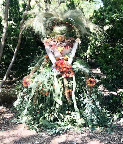 A woman scarecrow made of feathers and plants.